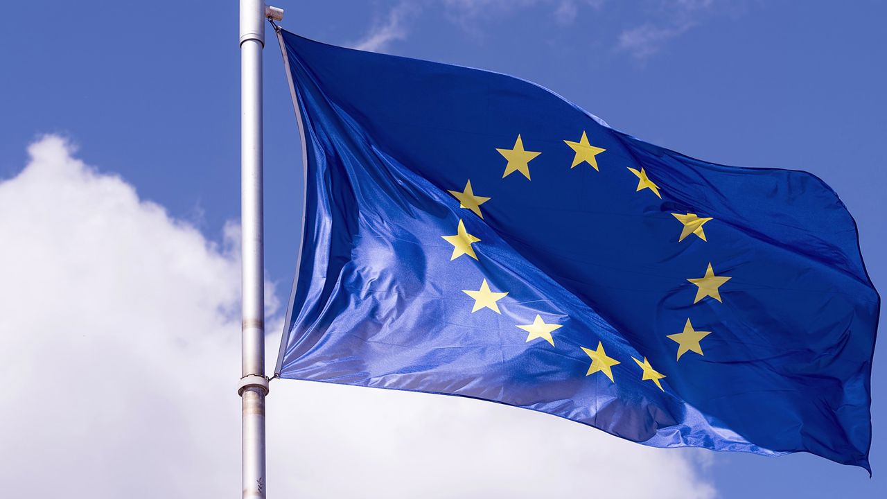Blå EU-flagga med gula stjärnor mot en blå himmel.