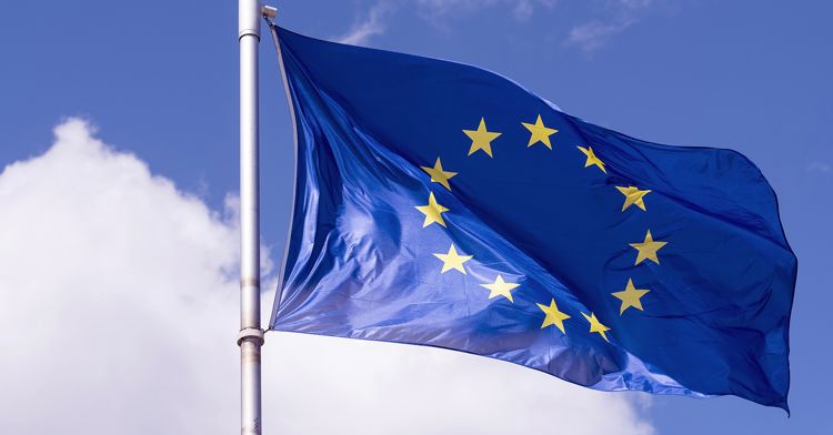 Blå EU-flagga med gula stjärnor mot en blå himmel.