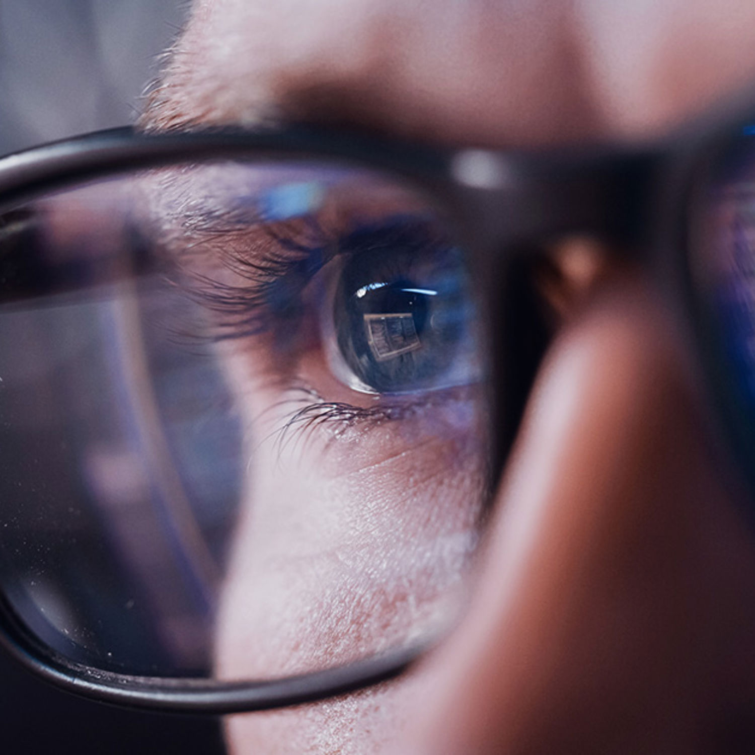 Närbild på person med glasögon, där man i glasögonen ser en reflektion från en datorskärm.