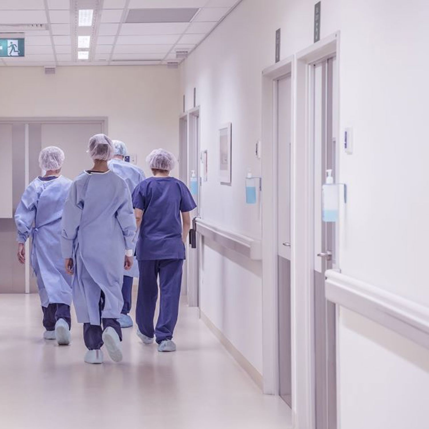 En grupp med vårdpersonal i blå sjukhusklädsel går bortåt i en korridor.