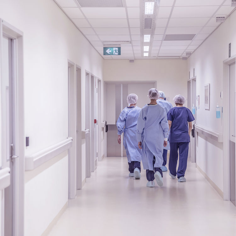 En grupp med vårdpersonal i blå sjukhusklädsel går bortåt i en korridor.